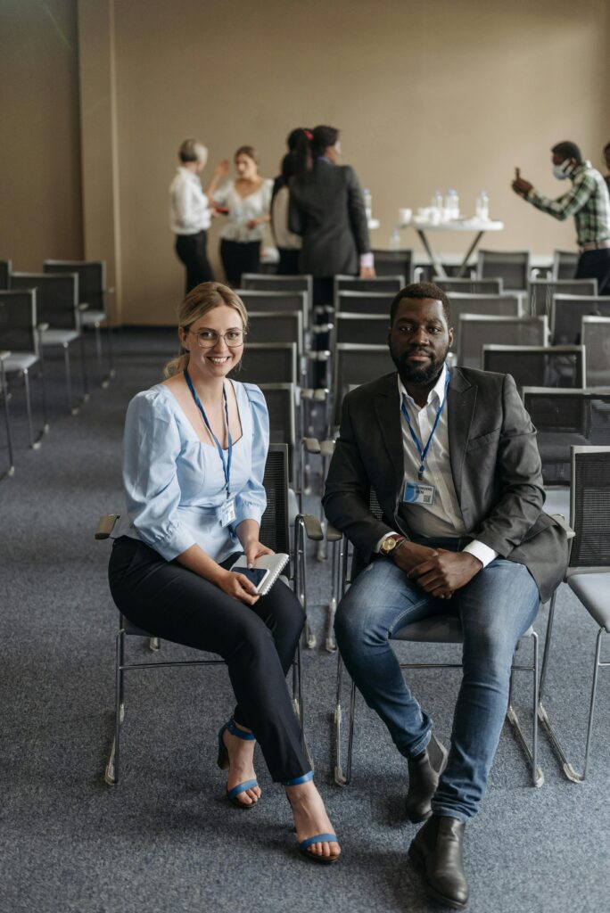 Two professionals sitting at a business conference, smiling and engaged.