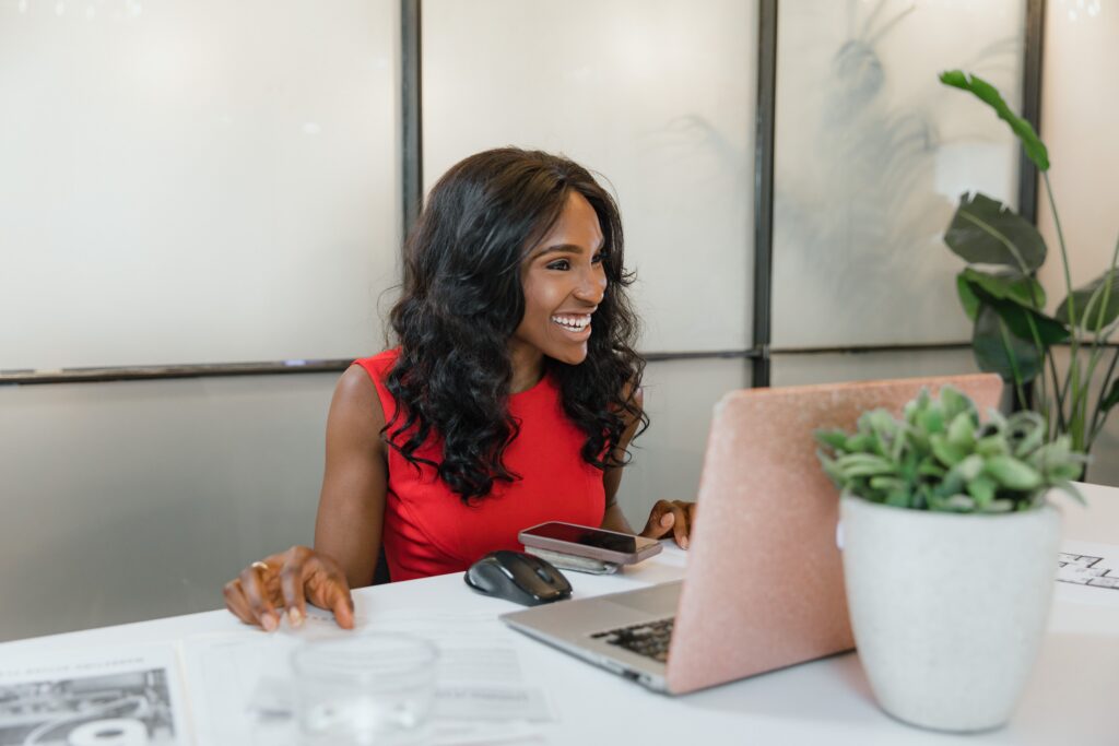 pexels photo 10375901 10375901 Professional black woman smiling at desk using laptop and smartphone in office.