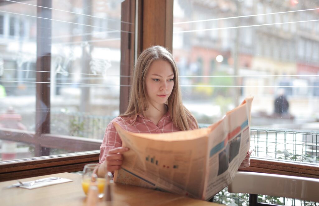 pexels photo 3928118 3928118 A young woman enjoying a newspaper at a cafe table, immersed in reading.