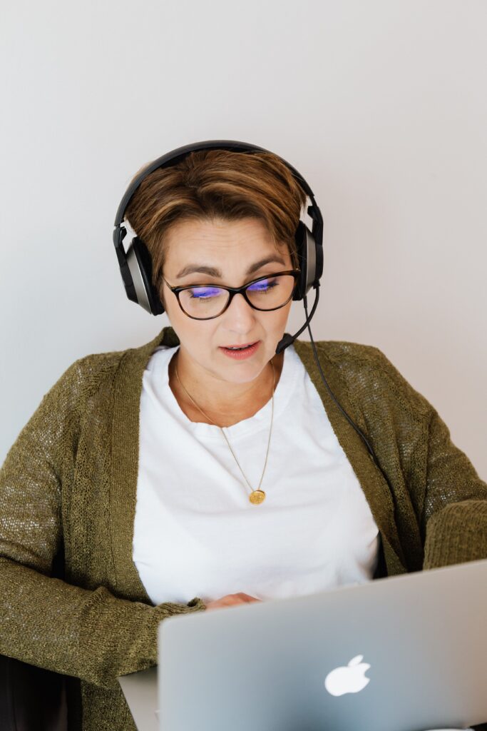 pexels photo 4468124 4468124 A woman working on a laptop indoors, wearing eyeglasses and headphones for focus and communication.