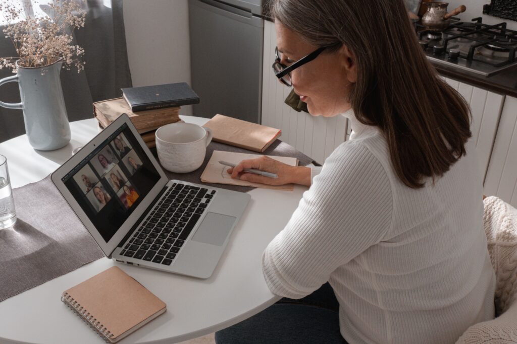 pexels photo 5486102 5486102 Adult woman participates in a video call, taking notes in a cozy indoor setting.