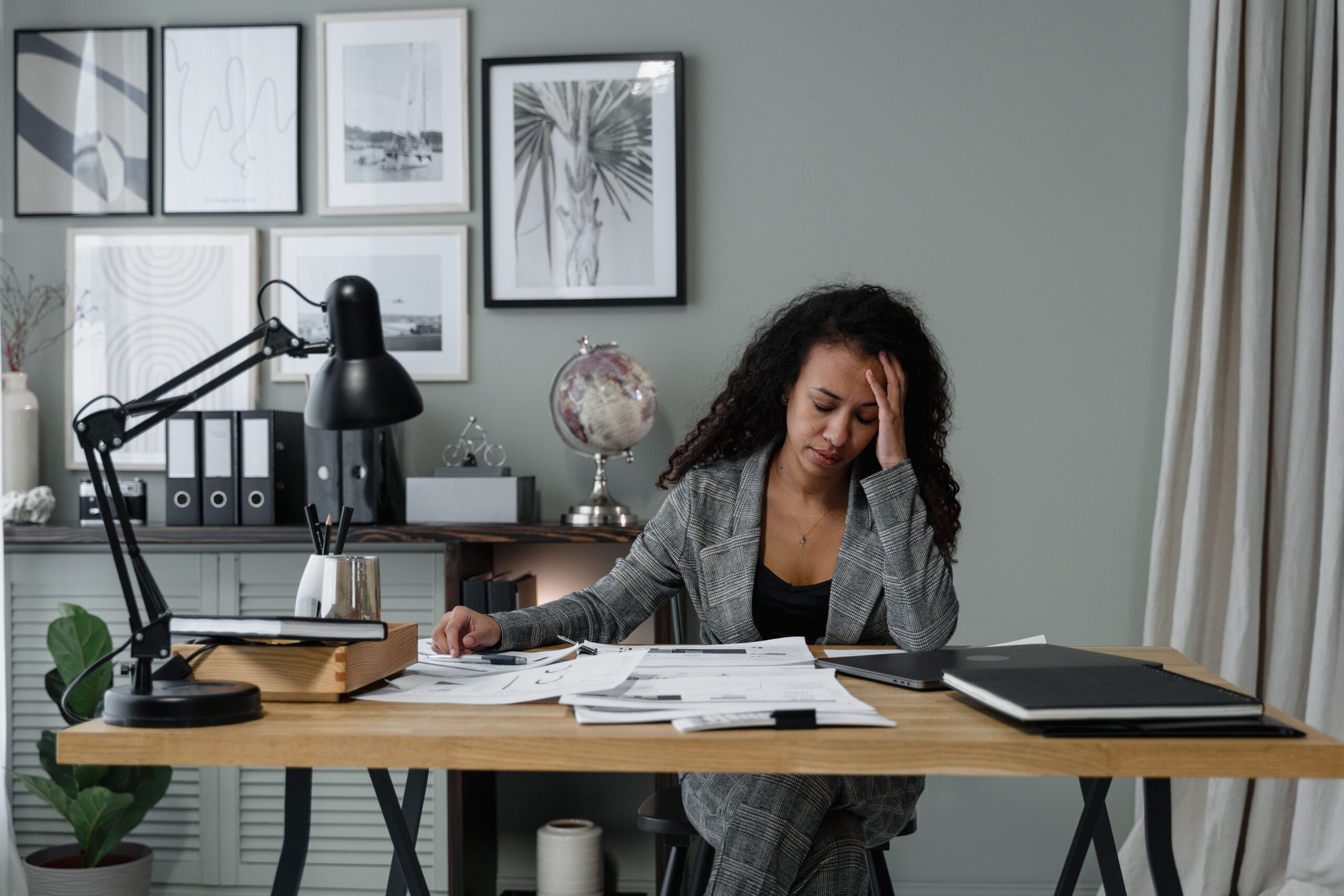 Businesswoman in a gray suit stressed at her office desk with documents and paperwork.