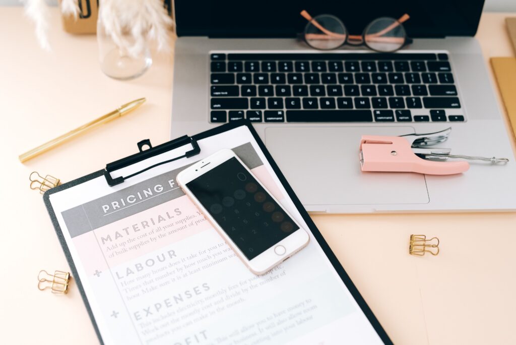 A stylish workspace featuring a laptop, smartphone, clipboard, and stationery essentials.